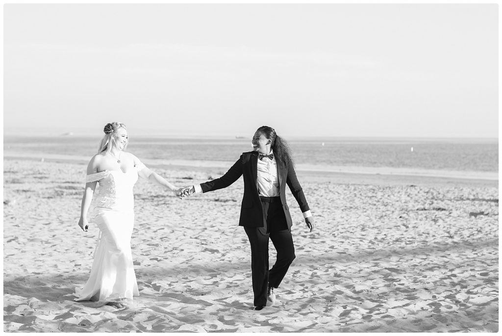 2 brides hand in hand walking on the beach