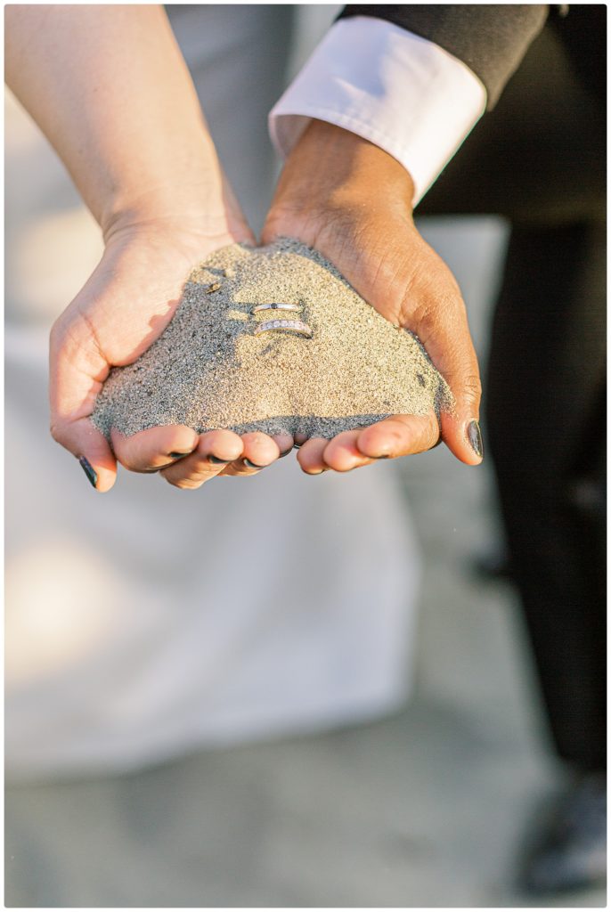 2 brides holding sand with their wedding rings neatly placed  in the sand