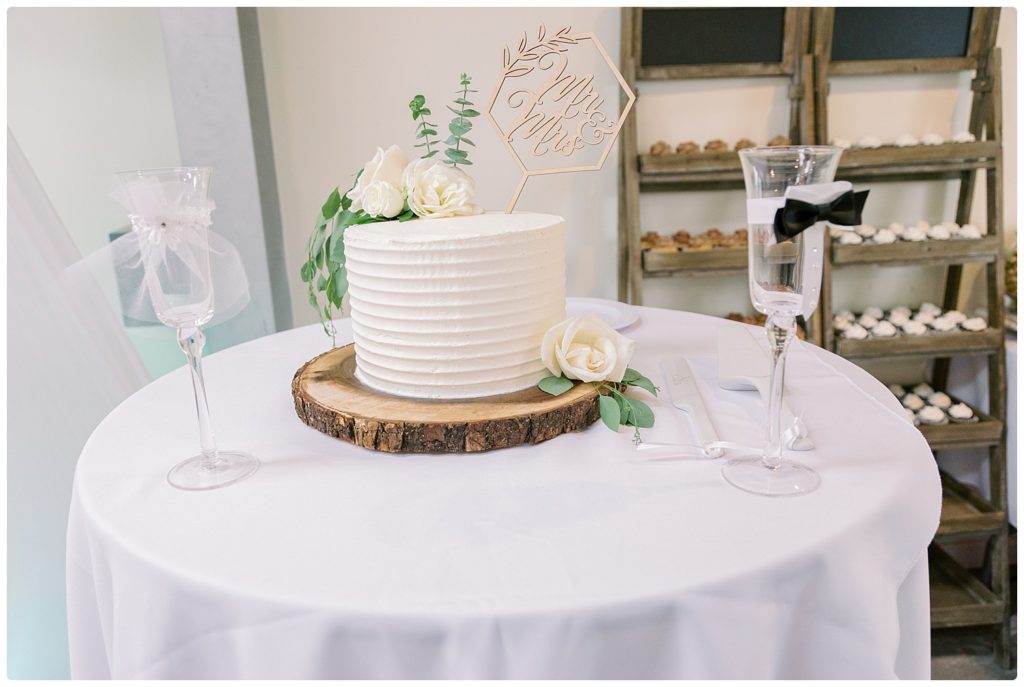 photo of wedding cake and 2 toasting glasses. One is wearing garter belt and one has bow tie at the center of the flute