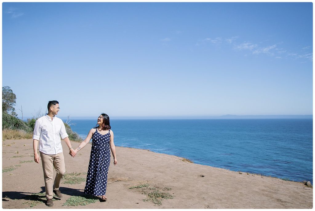 engagement couple walking along a beach cliff
