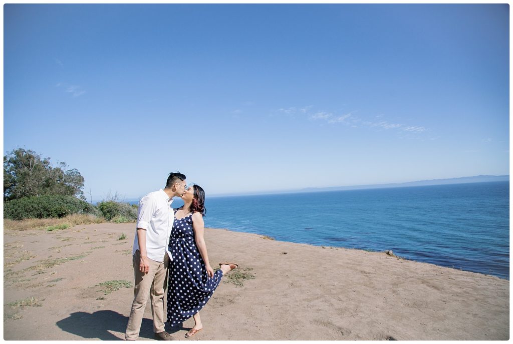 engagement couple kissing along a beach cliff - bride has one leg up