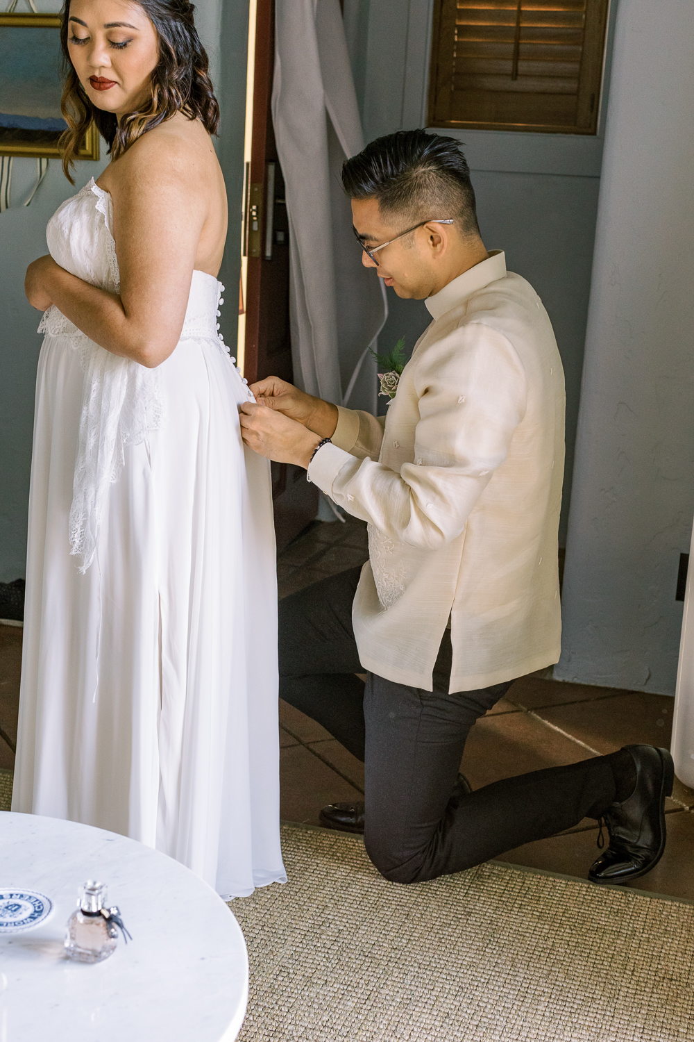 groom helping bride putting on wedding dress 2