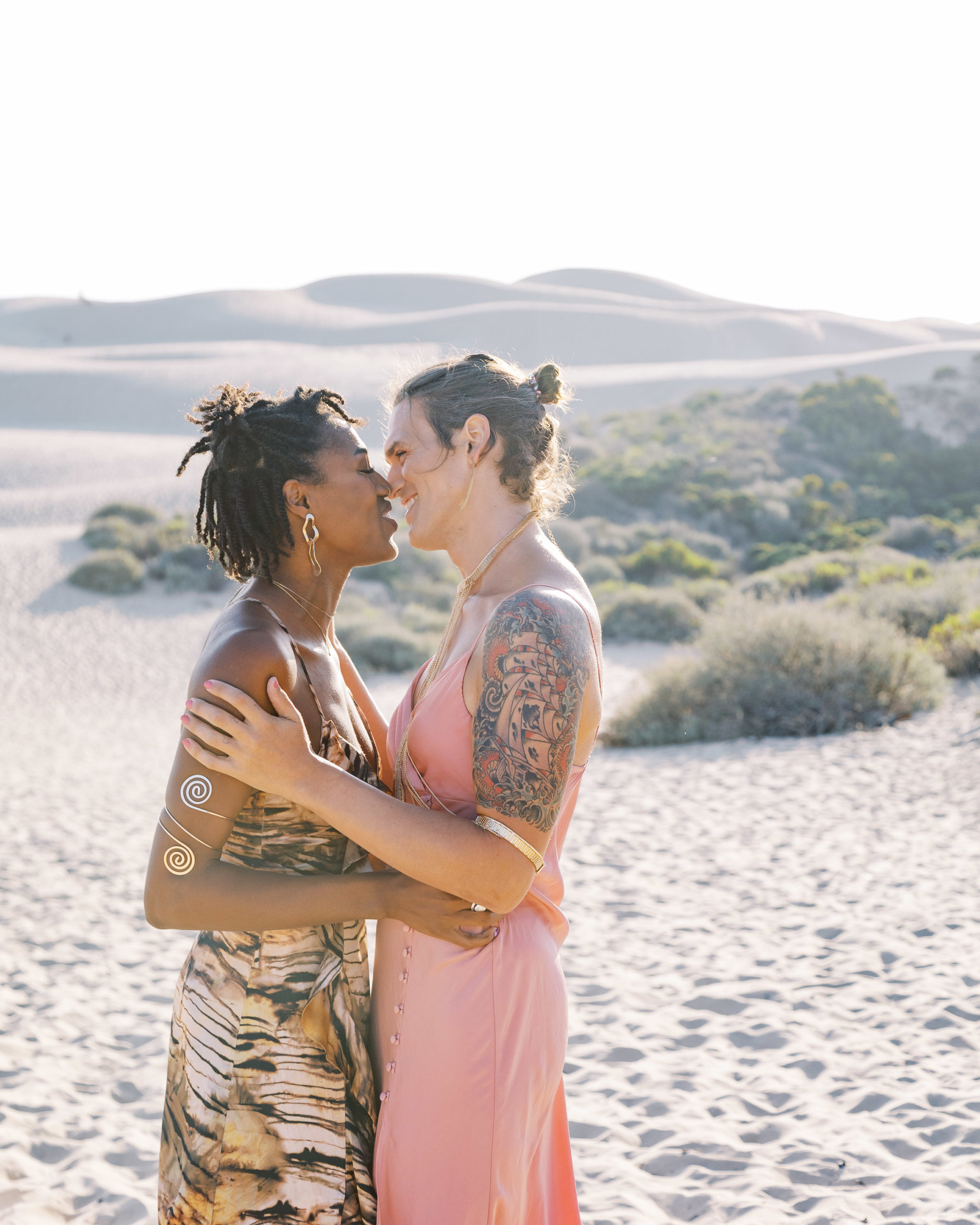 2 women in the sand lightly hugging captured by LGBT photographer
