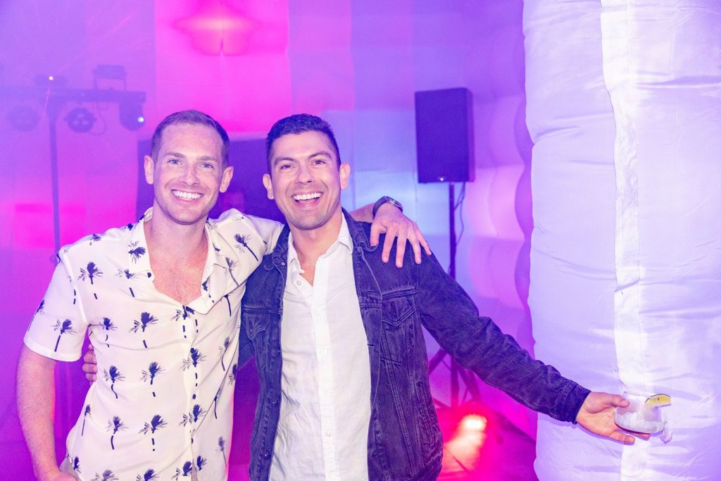 2 men arm around arm for a photo in a disco party tent
