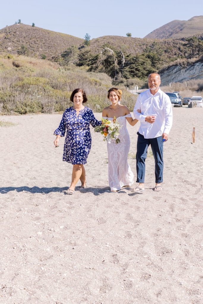 bride walking on the sand with her parents to get married