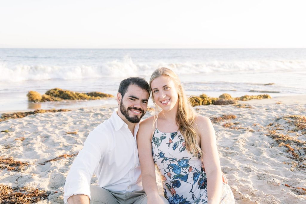 Engaged couple sitting on the sand for engagement photos
