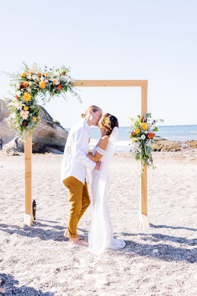 bride and groom kissing under beach wedding arch for boho wedding