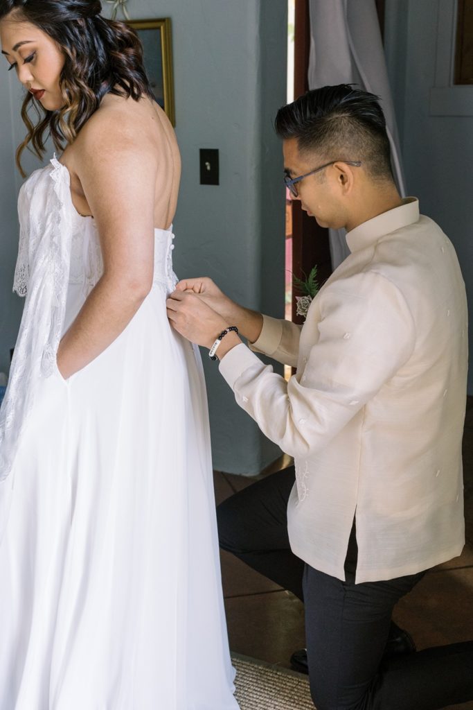 groom helping bride put on dress - getting ready picture